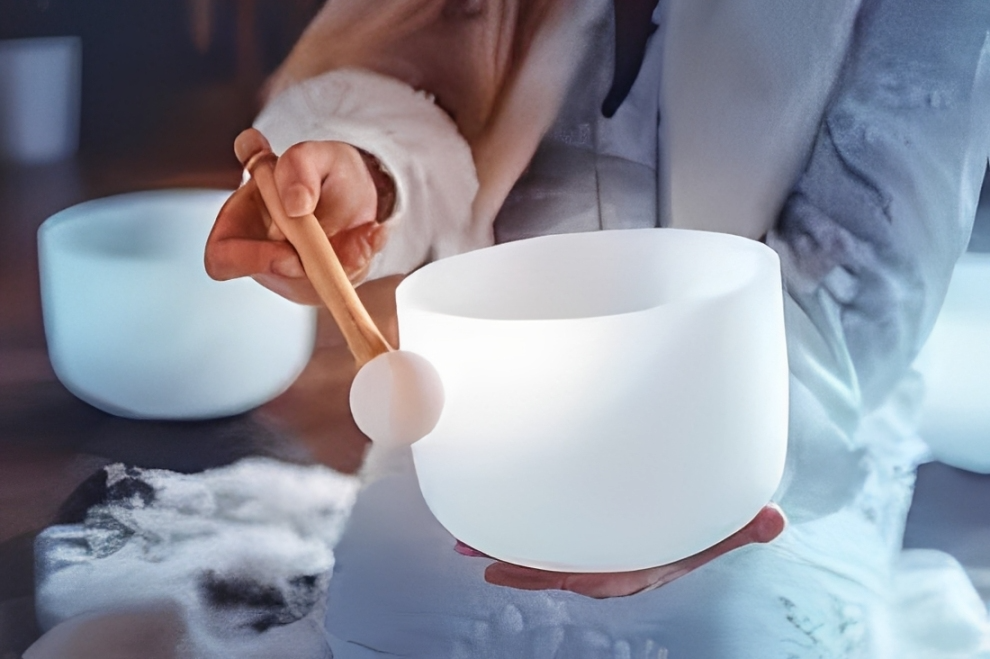 Person playing a white crystal singing bowl with a wooden mallet.