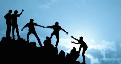 Silhouettes helping each other on mountain