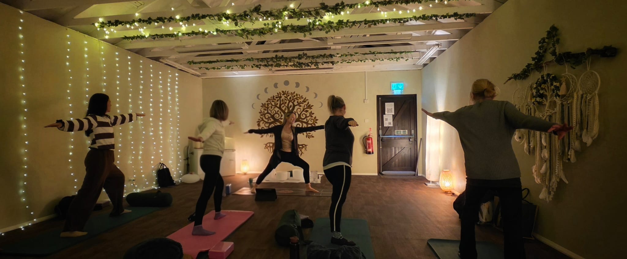 Three people practicing yoga in a cozy, dimly lit room with candles and wooden beams.